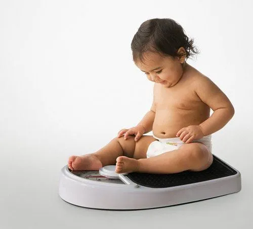 Bé 2 tuổi đang được đo cân nặng bởi người lớn, minh họa việc theo dõi sự phát triển thể chất.
